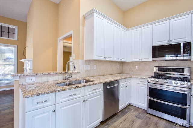 kitchen with kitchen peninsula, white cabinetry, light wood-type flooring, sink, and stainless steel appliances