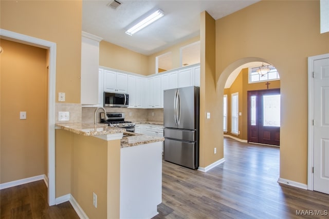 kitchen featuring hardwood / wood-style flooring, kitchen peninsula, stainless steel appliances, white cabinets, and light stone counters