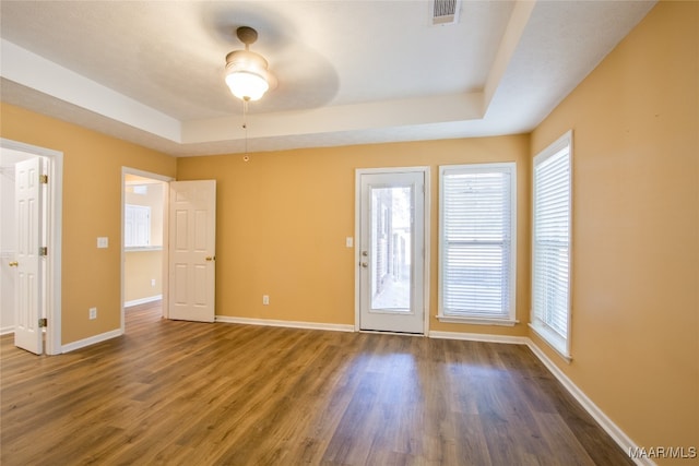 empty room with a raised ceiling, dark wood-type flooring, plenty of natural light, and ceiling fan