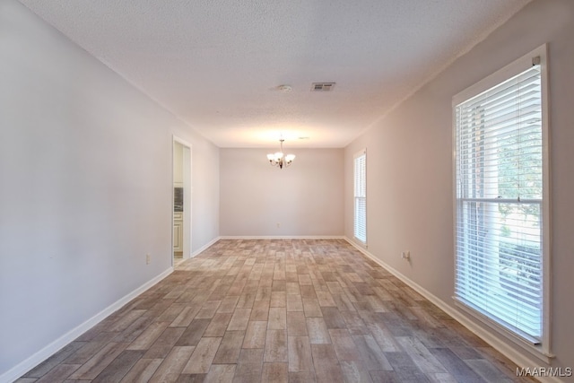 empty room featuring hardwood / wood-style floors, a notable chandelier, and a healthy amount of sunlight