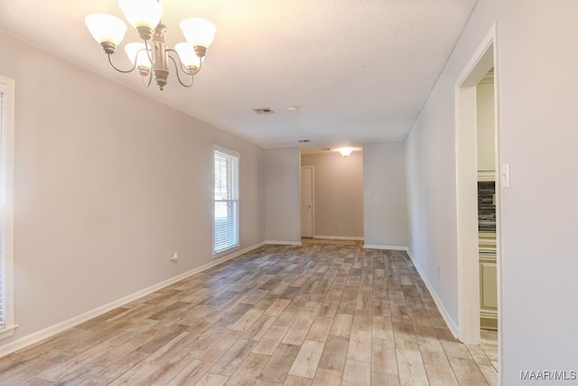 empty room featuring a textured ceiling, an inviting chandelier, and light wood-type flooring