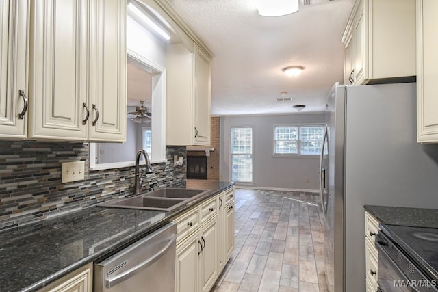 kitchen with cream cabinets, sink, dishwasher, ceiling fan, and dark stone countertops