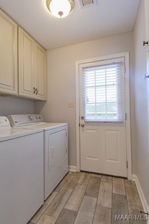 washroom featuring washer and dryer, a textured ceiling, cabinets, and light wood-type flooring