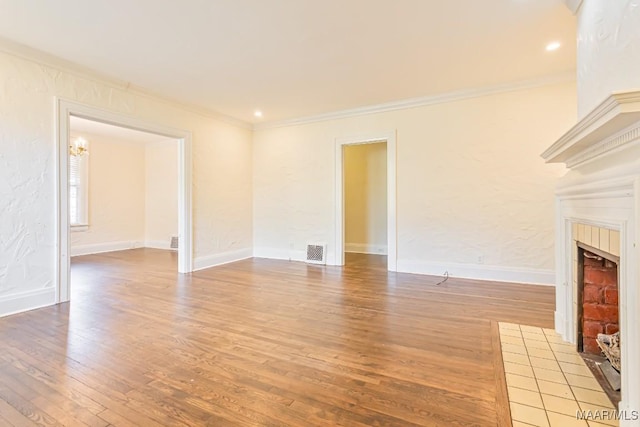 unfurnished living room featuring visible vents, crown molding, a tiled fireplace, wood finished floors, and baseboards