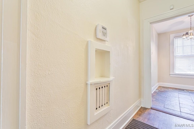 hallway featuring baseboards, a textured wall, wood finished floors, and a notable chandelier