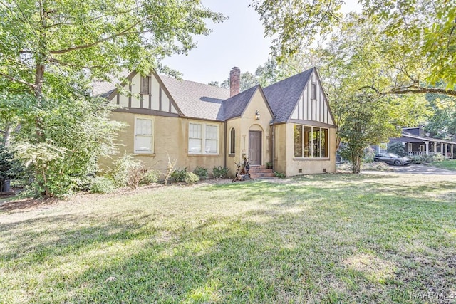tudor house featuring a chimney, a shingled roof, and a front yard