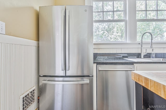 kitchen featuring appliances with stainless steel finishes, a healthy amount of sunlight, sink, and dark stone counters