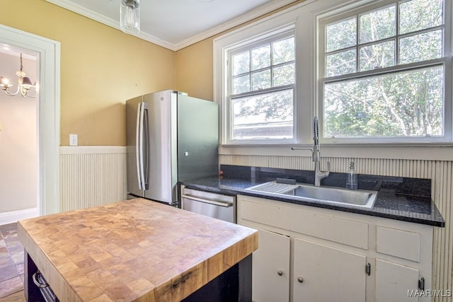 kitchen featuring a sink, an inviting chandelier, ornamental molding, stainless steel appliances, and white cabinetry
