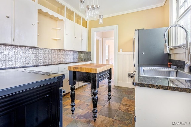 kitchen with white cabinets, a sink, decorative backsplash, ornamental molding, and stone tile flooring