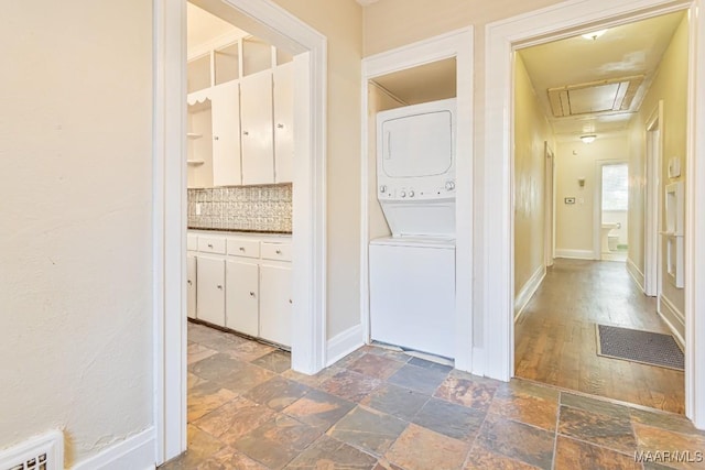 washroom with laundry area, stone tile floors, baseboards, attic access, and stacked washing maching and dryer