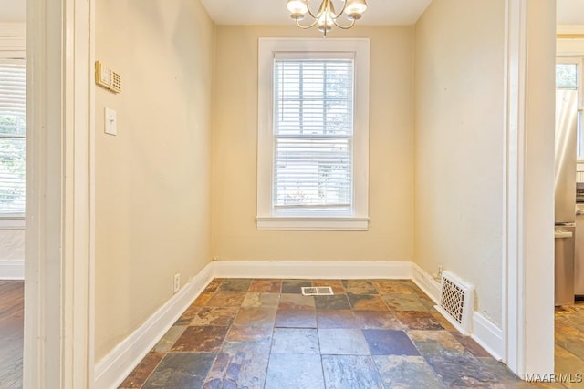 unfurnished dining area featuring baseboards, stone tile flooring, and visible vents