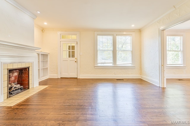 unfurnished living room featuring hardwood / wood-style flooring, a healthy amount of sunlight, ornamental molding, and a tile fireplace