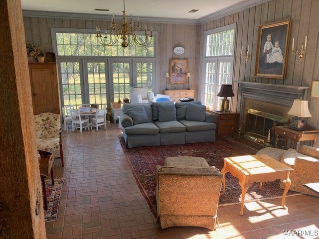 living room with an inviting chandelier, crown molding, wood walls, and a wealth of natural light