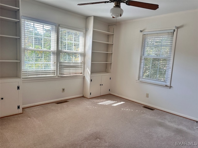 carpeted empty room featuring ceiling fan, crown molding, and a wealth of natural light