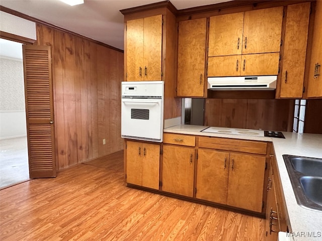 kitchen with wooden walls, ornamental molding, sink, light wood-type flooring, and white appliances