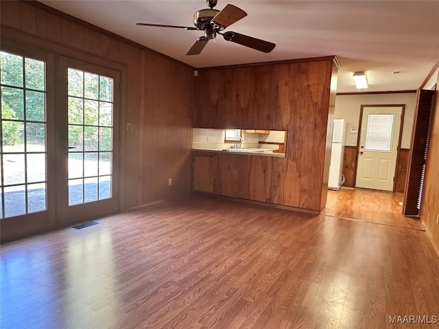 interior space featuring ornamental molding, ceiling fan, light hardwood / wood-style floors, and wood walls