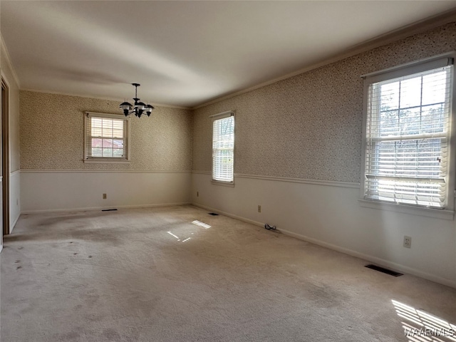 carpeted empty room with a wealth of natural light, a chandelier, and crown molding