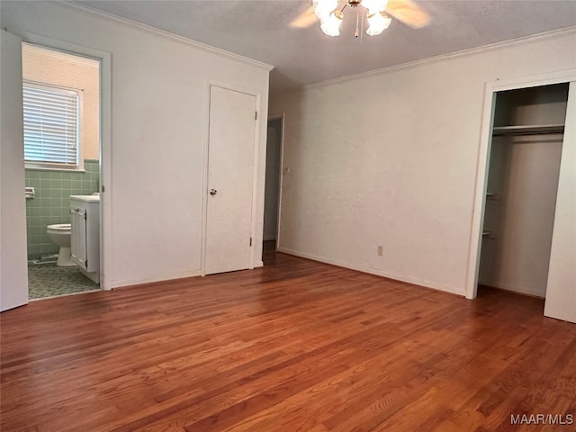 unfurnished bedroom with ceiling fan, hardwood / wood-style flooring, connected bathroom, tile walls, and ornamental molding