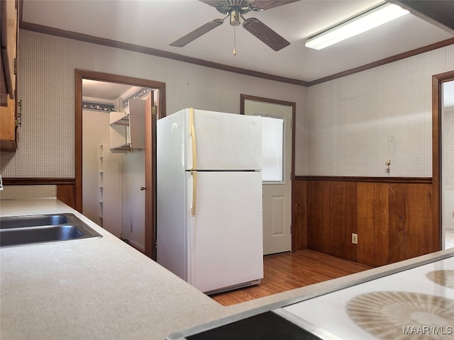 kitchen featuring light hardwood / wood-style flooring, wood walls, crown molding, sink, and white refrigerator