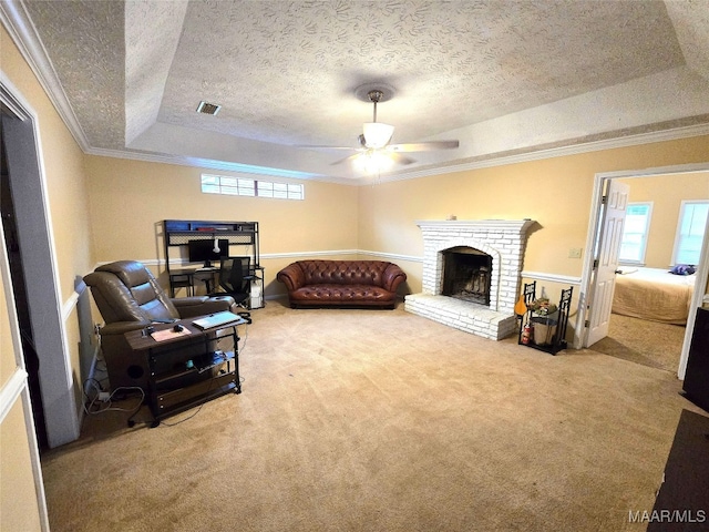 living room with a tray ceiling, a brick fireplace, carpet flooring, and ornamental molding