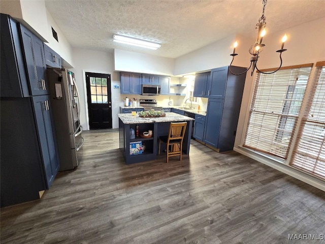 kitchen featuring dark hardwood / wood-style floors, blue cabinetry, appliances with stainless steel finishes, a kitchen island, and light stone counters