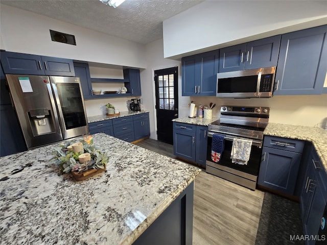 kitchen with light stone countertops, stainless steel appliances, blue cabinets, light hardwood / wood-style floors, and a textured ceiling