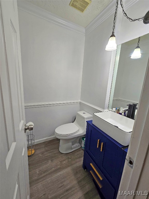 bathroom with vanity, a textured ceiling, crown molding, hardwood / wood-style floors, and toilet