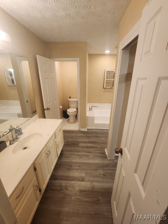 bathroom with vanity, toilet, a textured ceiling, wood-type flooring, and a tub