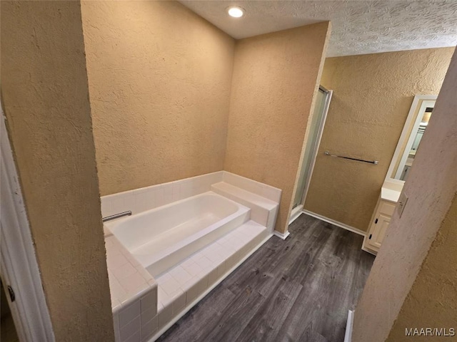 full bathroom with a stall shower, a textured wall, wood finished floors, a textured ceiling, and a bath