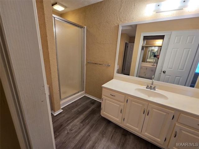 bathroom featuring a textured wall, a shower stall, vanity, and wood finished floors