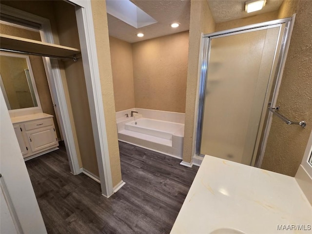 full bath featuring a skylight, a stall shower, wood finished floors, vanity, and a bath