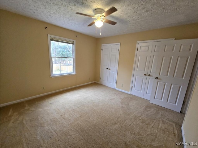 unfurnished bedroom featuring multiple closets, a ceiling fan, carpet flooring, a textured ceiling, and baseboards