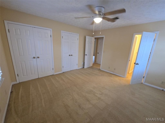 unfurnished bedroom with multiple closets, light colored carpet, a textured ceiling, and baseboards