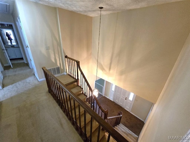 stairway featuring baseboards, visible vents, a textured ceiling, and carpet flooring