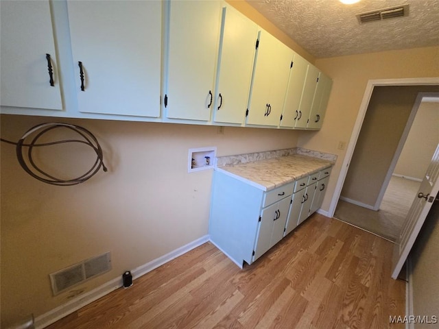 washroom featuring hookup for a washing machine, cabinet space, light wood-style floors, and visible vents