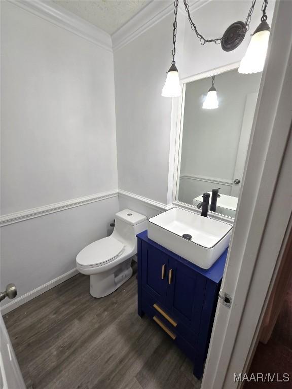 half bath with a textured ceiling, toilet, wood finished floors, vanity, and ornamental molding