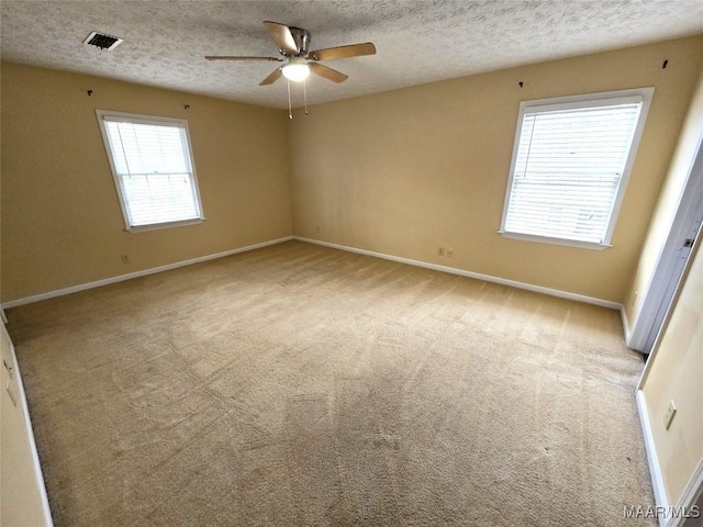 unfurnished room featuring light colored carpet, visible vents, a ceiling fan, a textured ceiling, and baseboards