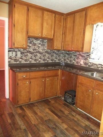 kitchen with dark wood-style floors, brown cabinets, tasteful backsplash, dark countertops, and a sink