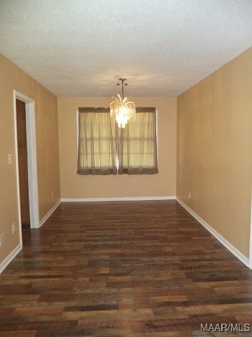 empty room with a chandelier, a textured ceiling, and dark hardwood / wood-style flooring