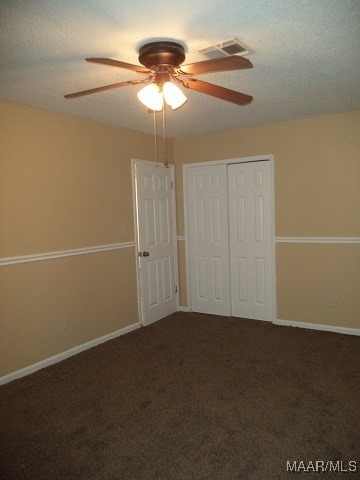 unfurnished bedroom featuring a closet, ceiling fan, a textured ceiling, and dark colored carpet