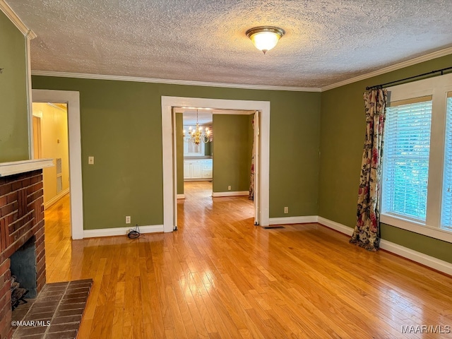 unfurnished living room featuring crown molding, a brick fireplace, a textured ceiling, light hardwood / wood-style floors, and a chandelier