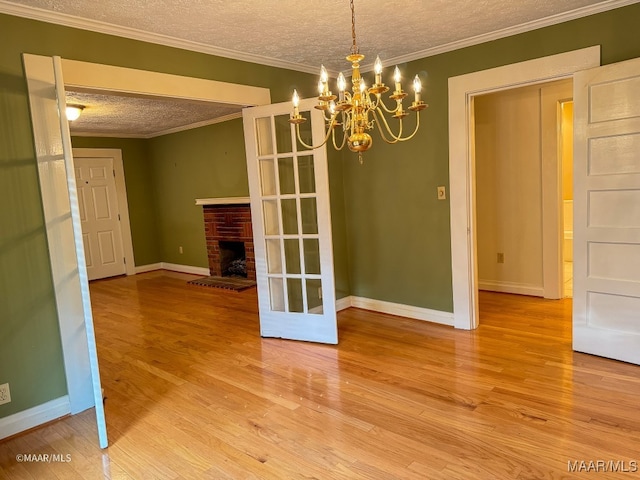 unfurnished dining area featuring a brick fireplace, hardwood / wood-style flooring, ornamental molding, a textured ceiling, and a chandelier