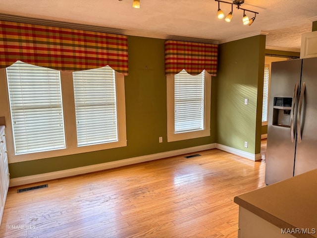 unfurnished dining area with light hardwood / wood-style floors, ornamental molding, and a textured ceiling