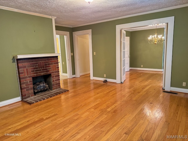 unfurnished living room with an inviting chandelier, ornamental molding, a fireplace, light wood-type flooring, and a textured ceiling