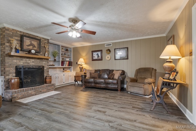 living room featuring hardwood / wood-style flooring, crown molding, a textured ceiling, a fireplace, and ceiling fan