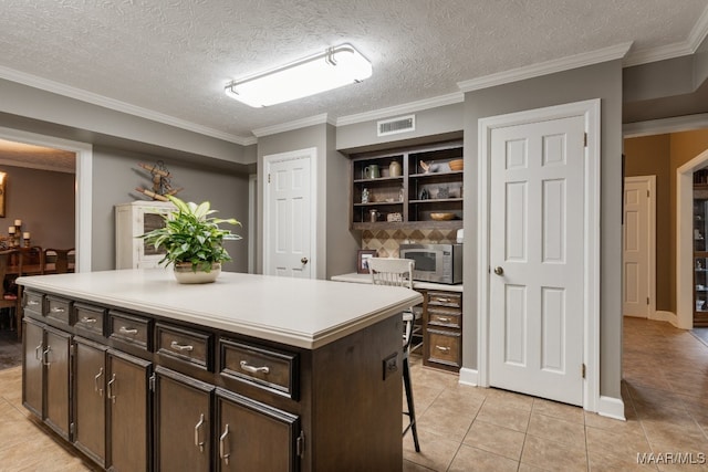 kitchen with a textured ceiling, light tile patterned floors, dark brown cabinets, and a kitchen island