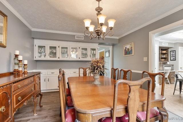 dining space featuring a notable chandelier, ornamental molding, a textured ceiling, and hardwood / wood-style floors