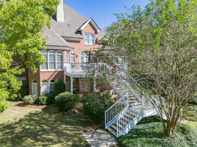 view of front of home with a shingled roof, stairs, a chimney, and brick siding