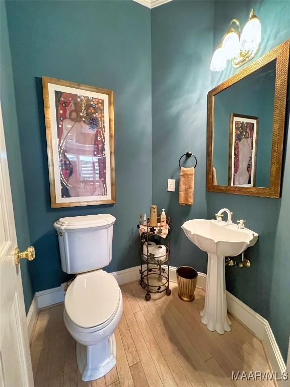 half bath with toilet, baseboards, and wood finished floors