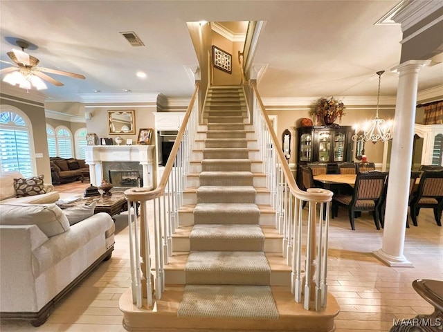 stairs featuring crown molding, ceiling fan with notable chandelier, decorative columns, and hardwood / wood-style flooring